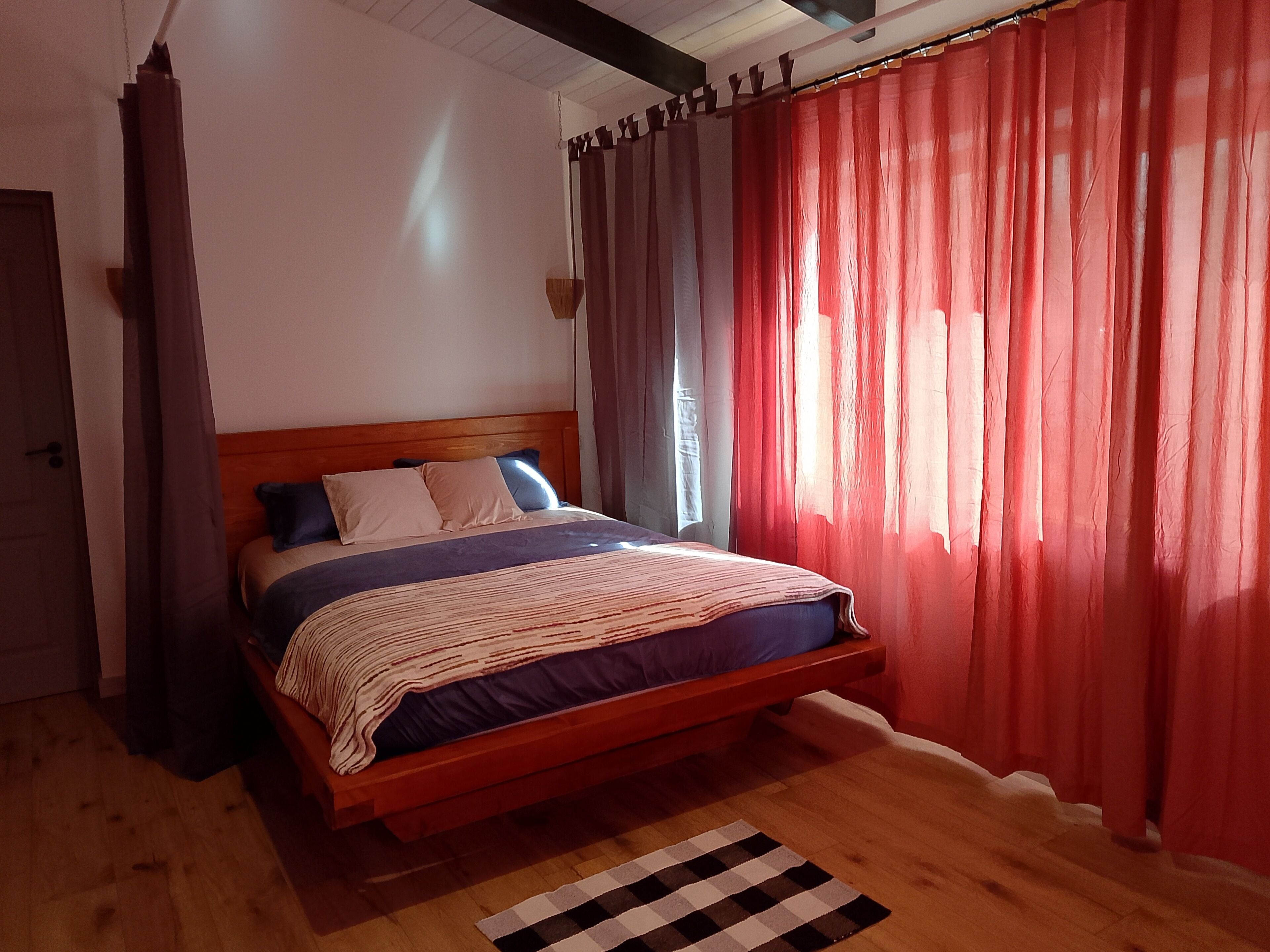 Una cama con estructura de madera, manta a rayas y dos almohadas.