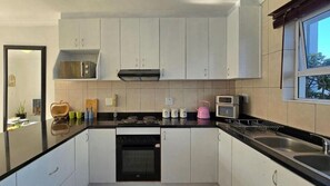 A modern kitchen with white cabinets, a black countertop, a microwave, a toaster, and a dish rack. - Steps from the Beach, Muizenberg Home (Cape Town)