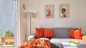 Ein modernes Wohnzimmer mit einem grauen Sofa, orangefarbenen Kissen, einer Stehlampe und zwei Wandbildern.