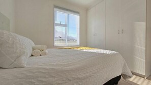 A bedroom with a bed, a window with blinds, and a wardrobe. - Steps from the Beach, Muizenberg Home (Cape Town)
