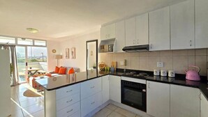 A modern kitchen with white cabinets, a black countertop, and a view of the outdoors. - Steps from the Beach, Muizenberg Home (Cape Town)