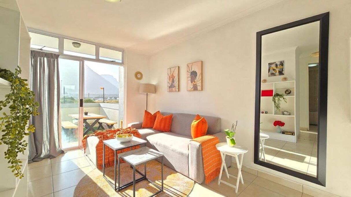 A modern living room with a sofa, coffee table, and a small side table. There is a large window with a view of mountains.