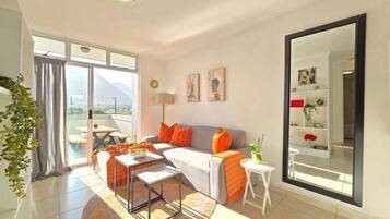 A modern living room with a sofa, coffee table, and a small side table. There is a large window with a view of mountains.