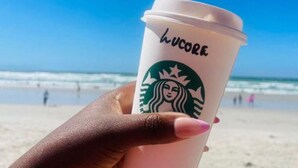 A hand holding a Starbucks cup with the word 'lucore' on it, standing on a beach with the ocean and people in the background. - Steps from the Beach, Muizenberg Home (Cape Town)