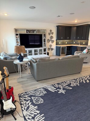 Ein modernes Wohnzimmer mit einem grauen Sofa, einem Fernseher und einer roten elektrischen Gitarre.