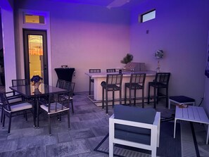 A patio area with a dining table, chairs, a bar counter, and a grill. - Newly built 4-bed house in Esplanade by the Islands BOAT INCLUDED with captain. (Naples)