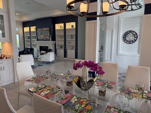 A modern dining area with a glass table set for six, surrounded by white chairs. - Newly built 4-bed house in Esplanade by the Islands BOAT INCLUDED with captain. (Naples)