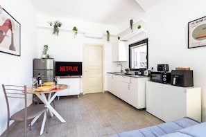 A modern kitchen with white cabinetry, a dining area with a table set for two, and a television displaying 'NETFLIX'. - [5 min from the M1 subway] Private Suite - CityLife (Milano)