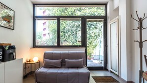 Ein modernes Wohnzimmer mit einer Couch, einer Kaffeemaschine, einer Lampe und einem großen Fenster mit Blick auf Grünflächen.