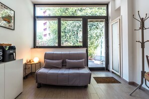 A modern living room with a sofa, a coffee machine, a lamp, and a large window with a view of greenery. - [5 min from the M1 subway] Private Suite - CityLife (Milano)