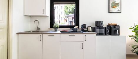 A modern kitchen with white cabinetry, a window with a view of buildings, and various appliances.