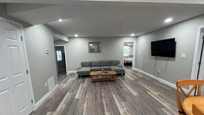 Ein Wohnzimmer mit einem grauen Ecksofa, einem Holztisch und einem an der Wand montierten Fernseher.