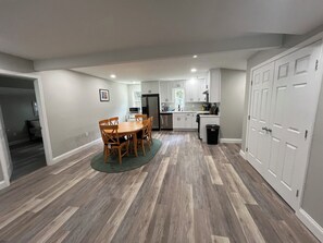 A compact kitchen with white cabinets, a dining table with chairs, and a trash bin. - 3-bedroom house in beautiful Cove point Beach! Just a short walk from the beach (Lusby)