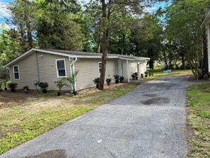 A single-story house with a covered porch, a driveway, and a small garden with various potted plants. - 3-bedroom house in beautiful Cove point Beach! Just a short walk from the beach (Lusby)