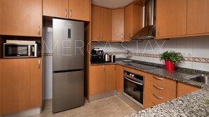A kitchen with wooden cabinets, a stainless steel refrigerator, a microwave, a stove, and a sink. - Beautiful, centrally located apartment (Sitges)