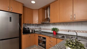 A modern kitchen with wooden cabinets, stainless steel appliances, a granite countertop, and a built-in oven. - Beautiful, centrally located apartment (Sitges)