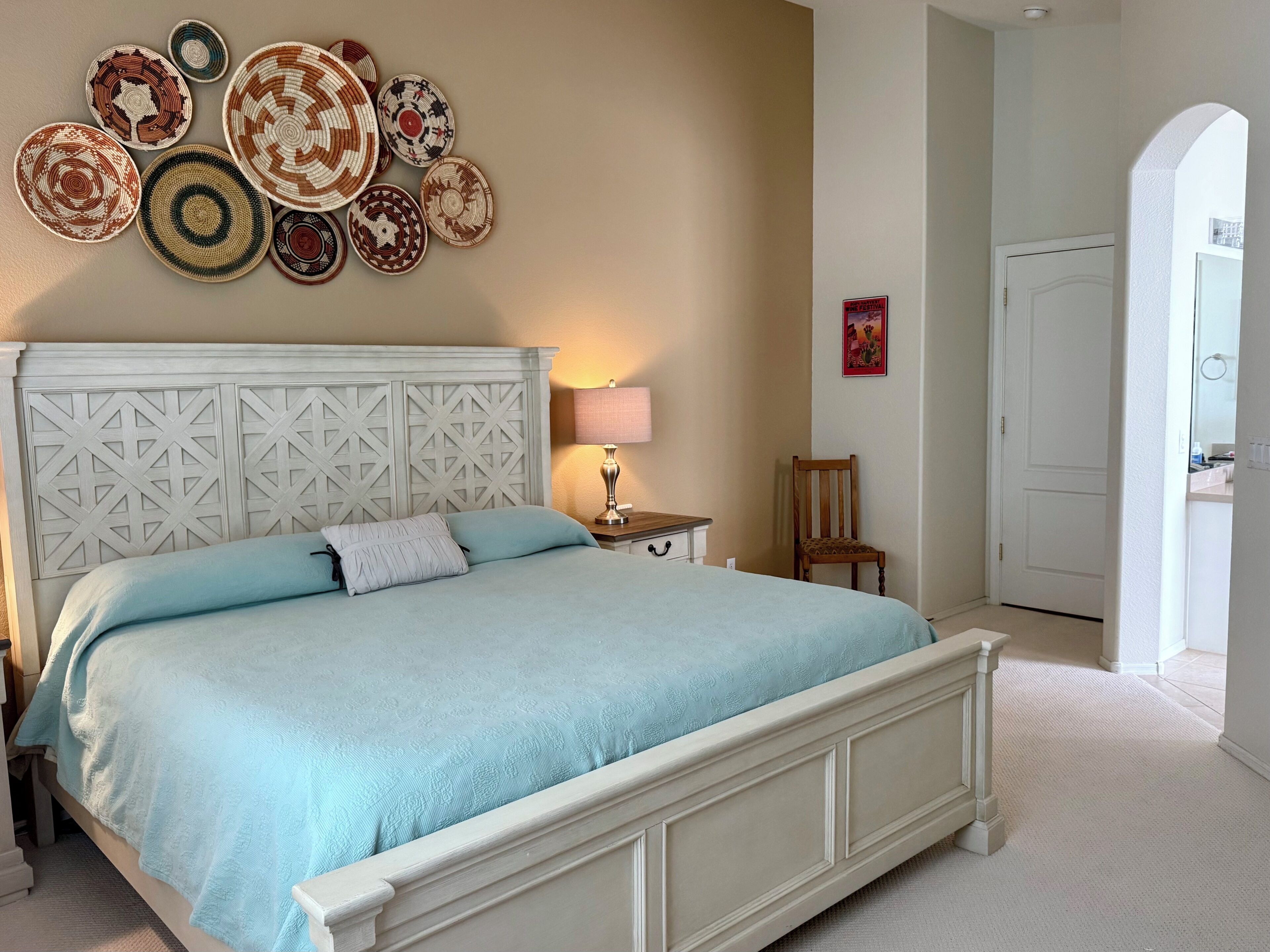 Une chambre à coucher comprenant un lit, une table de chevet, une lampe, une chaise et un mur décoré d’assiettes.