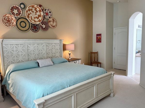 Un dormitorio con cama, mesita de noche, lámpara, silla y un muro decorado con platos.