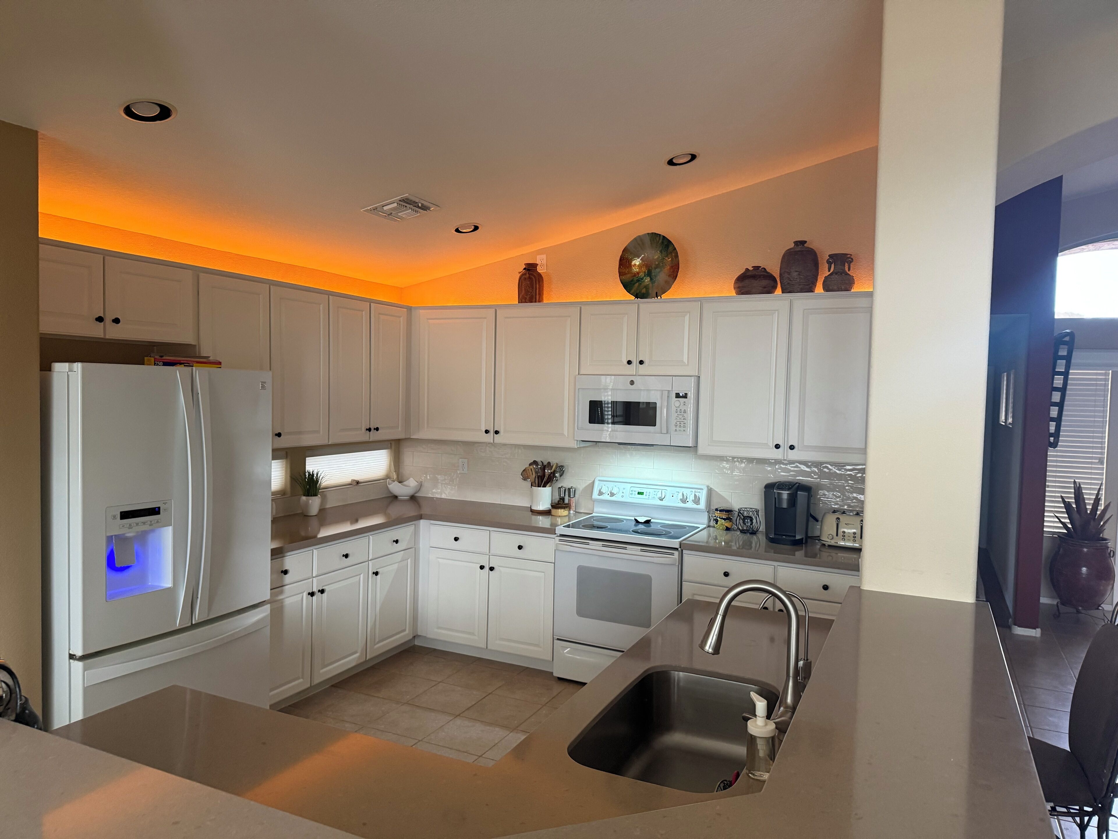 Una cocina moderna con armarios blancos, un lavamanos de acero inoxidable, un microondas integrado y una estufa.