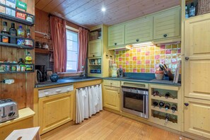 A kitchen with wooden cabinets, a built-in oven, a sink, and various kitchen appliances. - Praz de la Legettaz C & D – Stunning Duplex with Panoramic Views (Val-d'Isère)