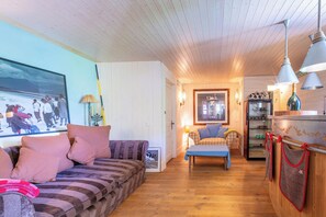 A cozy living room with a sofa, a table, and a kitchen area with a refrigerator and a hanging oven mitt. - Stunning Duplex with Panoramic Views, ski in ski out (Val-d'Isère)