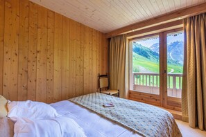 A wooden room with a bed, a chair, and a window with a view of a mountain landscape. - Stunning Duplex with Panoramic Views, ski in ski out (Val-d'Isère)