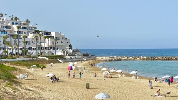 Une plage avec des gens, des parasols et un immeuble à plusieurs étages.