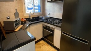 Une cuisine compacte équipée d’un réfrigérateur noir, d’une cuisinière à gaz, d’un four encastré et d’un grille-pain.
