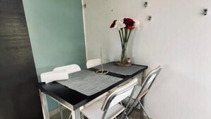 Un pequeño comedor con una mesa y sillas, un florero con flores y una pared azul claro.