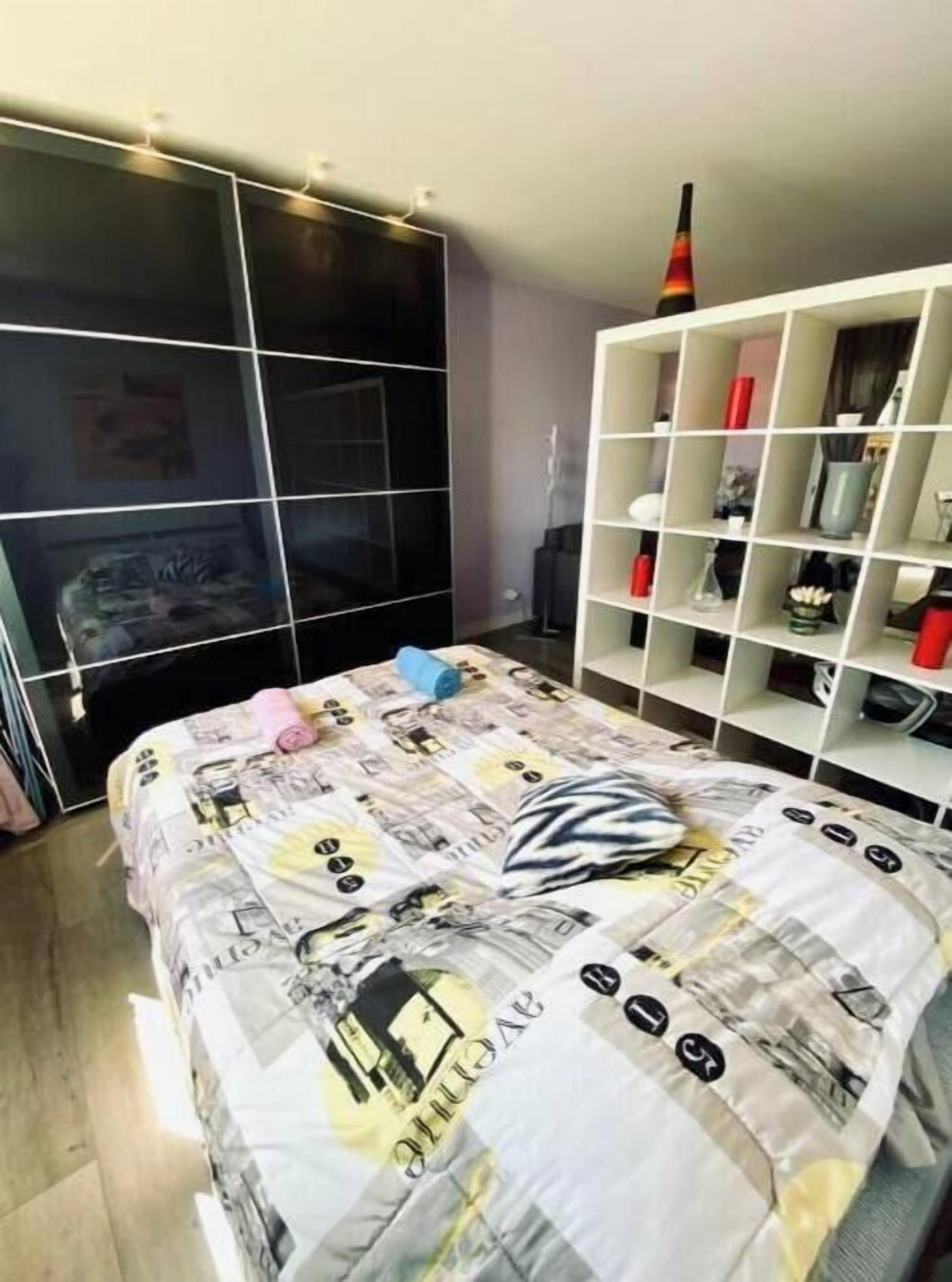 A bedroom with a bed, a wardrobe, and a white shelving unit.