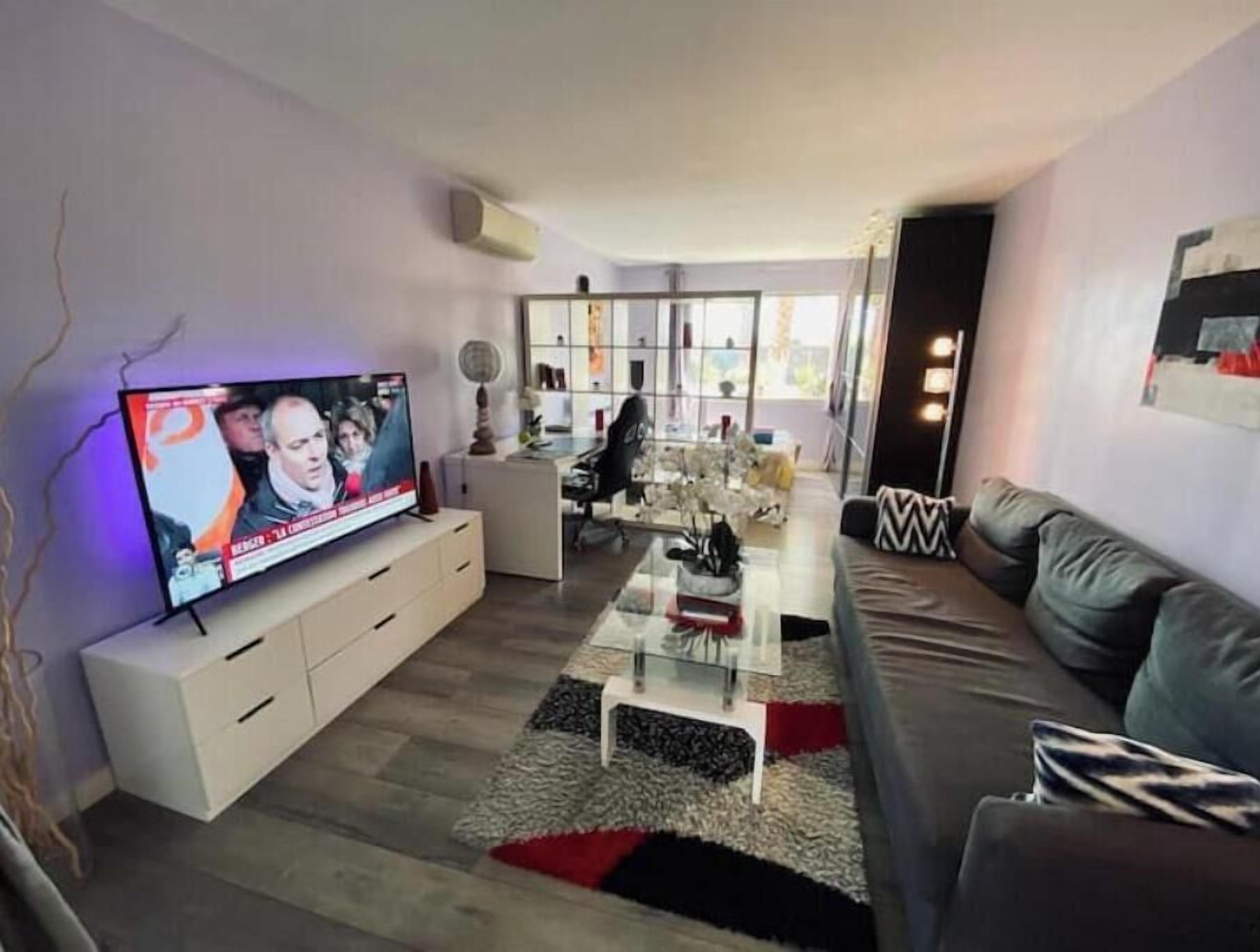 Un salon moderne avec un téléviseur à écran plat, un canapé, une table basse et une cloison en verre.