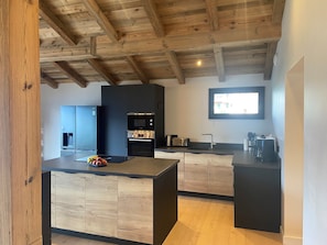 Eine moderne Küche mit Holzbalken, einem eingebauten Backofen und einer großen Kochinsel.