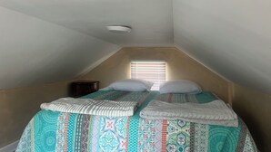 A small, single-bed room with a sloped ceiling, a window with blinds, and a ceiling light fixture. - The Dutchmen 420 Friendly. Loft tiny house  (Ocean View)