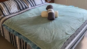 Una cama con ropa de cama a rayas, una manta verde y un cojín con un diseño de pájaro.