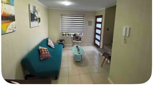 Una sala de estar con sofá, una mesa de centro, una ventana con persianas y una puerta.