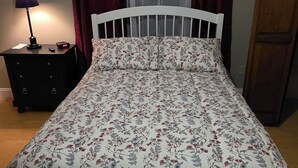 Ein Schlafzimmer mit einem Bett, einem Nachttisch, einer Lampe, einem Fenster mit Vorhängen und einem Holzschrank.