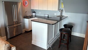 Una cocina moderna con refrigerador de acero inoxidable, gabinetes blancos, encimera negra y una isla integrada con taburetes.