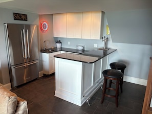 Eine moderne Küche mit einem Edelstahl-Kühlschrank, weißen Schränken, einer schwarzen Arbeitsplatte und einer integrierten Kücheninsel mit Hockern.