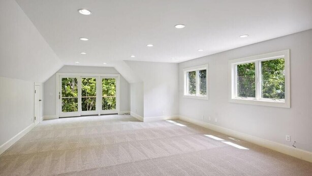 Una habitación amplia con ventanas grandes, techo inclinado y piso alfombrado.