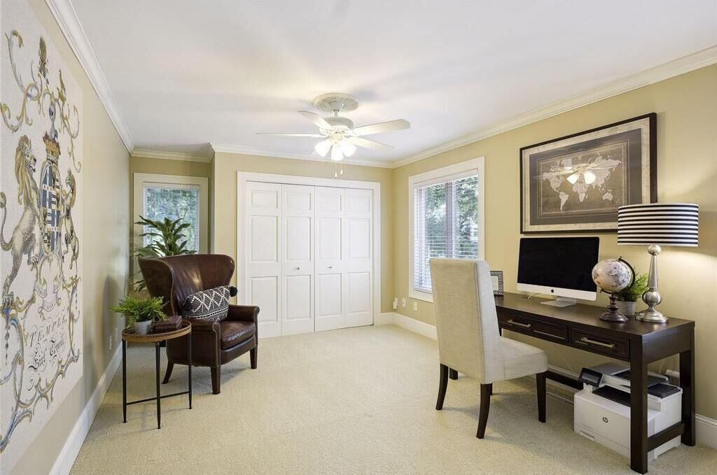 A room with a ceiling fan, a desk with a computer, a chair, a bookshelf, and a door.