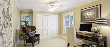 A room with a ceiling fan, a desk with a computer, a chair, a bookshelf, and a door.