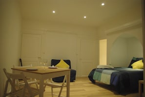 A room with a dining table, two chairs, a bed with a blue and green bedspread, and a white door. - Dijon Standing Historic City Apartment (Dijon)