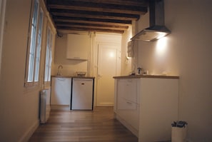 A narrow hallway with wooden flooring, a white door at the end, and a small kitchenette with a sink and a stove. - Dijon Standing Historic City Apartment (Dijon)