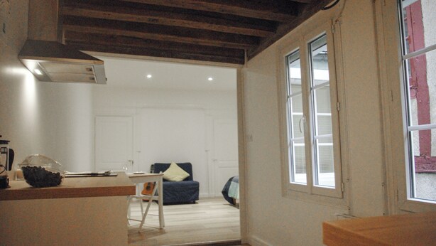 Ein Zimmer mit Holzboden, einem Fenster, einer Küchenzeile und einer Sitzecke mit Sessel und Sofa.