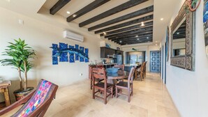 A dining area with a table and chairs, a potted plant, and a wall-mounted air conditioner. - CCV - 2BR Ocean-View Condo w/ Balcony, Golf & Pools at Quivira - Cabo San Lucas (Cabo San Lucas)