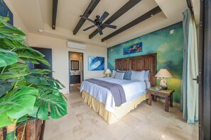 A bedroom with a bed, a nightstand, a ceiling fan, and a large plant. - CCV - 2BR Ocean-View Condo w/ Balcony, Golf & Pools at Quivira - Cabo San Lucas (Cabo San Lucas)