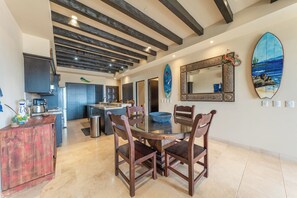 A modern kitchen with dark wooden beams, a dining area with a glass table, and a large decorative mirror. - CCV - 2BR Ocean-View Condo w/ Balcony, Golf & Pools at Quivira - Cabo San Lucas (Cabo San Lucas)