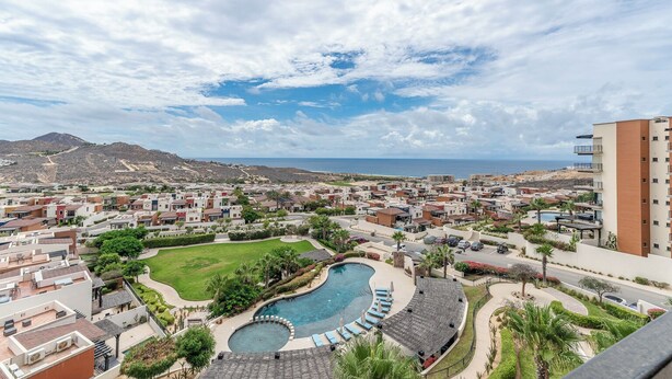 A residential area with a swimming pool, a view of the sea, and a mountain in the background. - CCV - 2BR Ocean-View Condo w/ Balcony, Golf & Pools at Quivira - Cabo San Lucas (Cabo San Lucas)