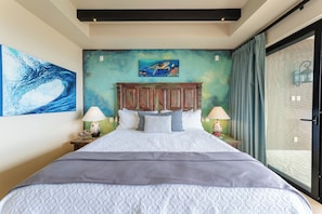 A bedroom with a bed, two bedside tables, a headboard, a painting, and a view through a sliding door. - CCV - 2BR Ocean-View Condo w/ Balcony, Golf & Pools at Quivira - Cabo San Lucas (Cabo San Lucas)