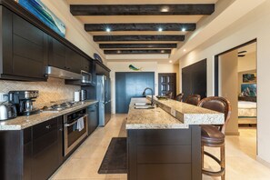 A modern kitchen with dark cabinetry, a granite countertop, and a central island with bar stools. - CCV - 2BR Ocean-View Condo w/ Balcony, Golf & Pools at Quivira - Cabo San Lucas (Cabo San Lucas)